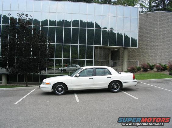 1998 Ford Crown Victoria parked in a lot in front of a modern building with reflective windows