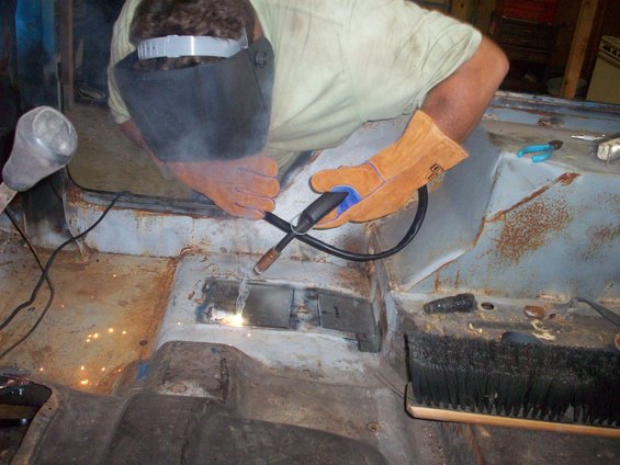 person welding rusted floor of vehicle interior