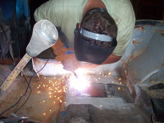 Welder in mask and gloves repairs rusted vehicle floor with sparks flying