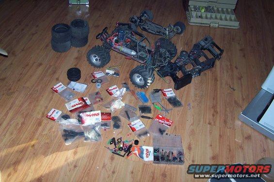 Several disassembled remote control vehicles and piles of parts are scattered on a wooden floor