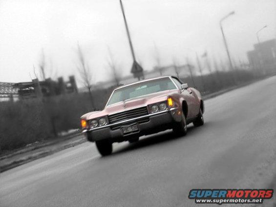 Pink 1970s Cadillac Coupe de Ville driving on a road