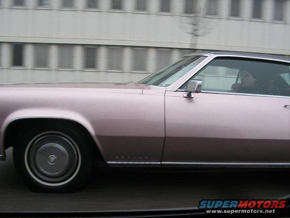 Side view of a pink Cadillac Eldorado driving past a building