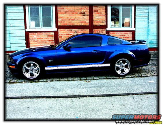 Blue 2005 Ford Mustang GT parked on a cobblestone street in front of a brick building