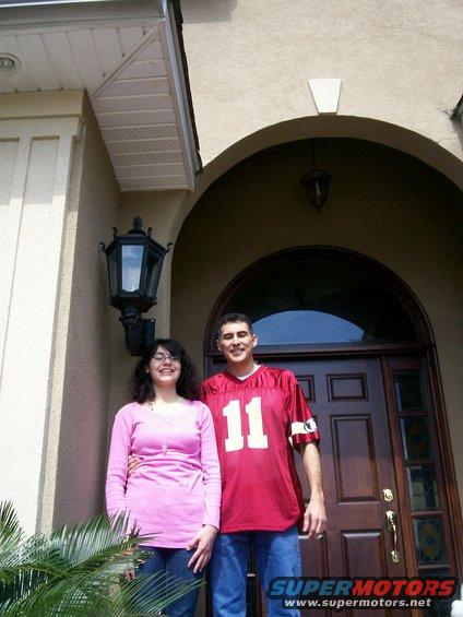 Couple in front of a dark wood door with arched window above. Man wears a red jersey with number 11