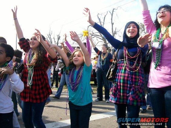 Crowd of people with arms raised, wearing Mardi Gras beads