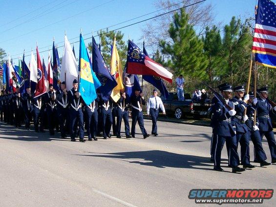 Parade with flags and military personnel marching, a pickup truck in the background