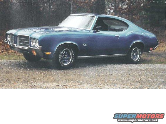 Blue coupe with chrome grille and trim, parked on gravel
