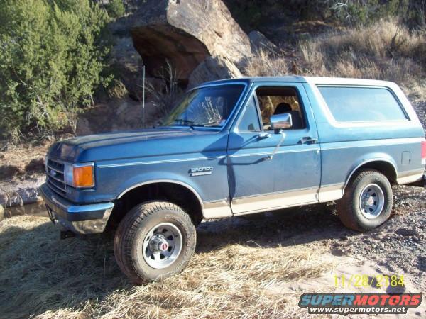 Blue 1990 Ford Bronco with a white top parked on a dirt road