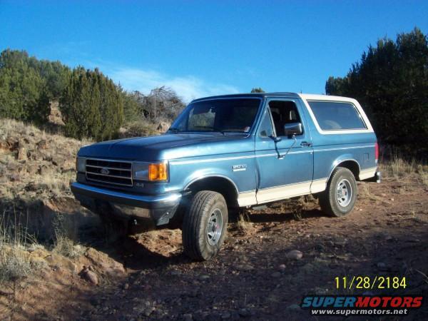 1990 Ford Bronco parked on dirt road with trees and hills in background