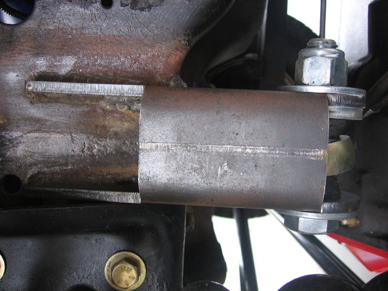 Close-up of a welded metal bracket attached to a vehicle's suspension system with bolts and washers