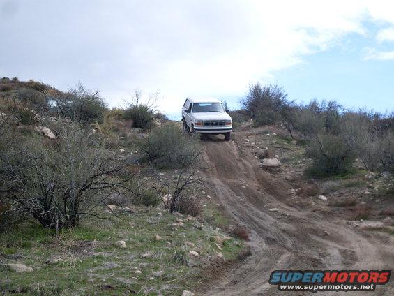 White 1992 Ford Bronco climbing a steep dirt trail with scrub brush and rocks