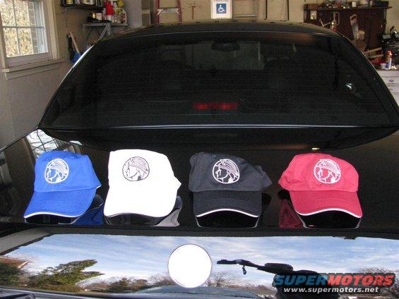 Four baseball caps (blue, white, black, red) with a Mercury Marauder logo on a black car trunk