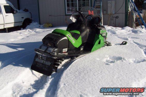 Green and black snowmobile with "ARCTIC CAT" text on the side, partially buried in snow