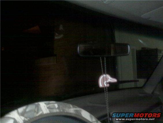 Interior shot of a vehicle, showing the rearview mirror and a duck-shaped air freshener hanging from it. Part of the steering wheel is visible