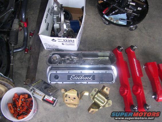 Engine valve covers, lifters, and suspension components laid out on a concrete floor
