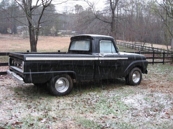 Black 1966 Ford F-100 pickup truck in light snow