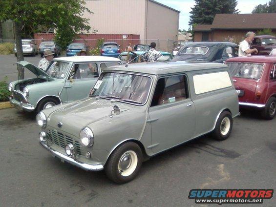 Gray Mini Cooper panel van parked next to a light green Mini Cooper with its hood up and a red Mini Cooper