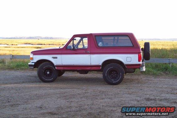 Side view of a red and white 1995 Ford Bronco parked on a dirt road