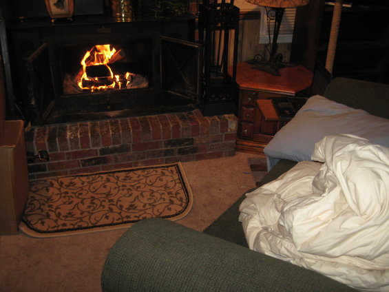fireplace with burning logs, brick hearth, rug, and part of a couch with blankets