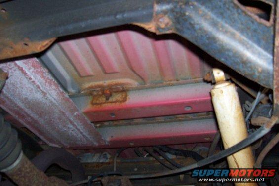 Underside of vehicle frame showing rust and a shock absorber