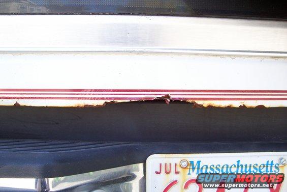 close-up of rust on lower body panel with red and white stripes, Massachusetts license plate visible