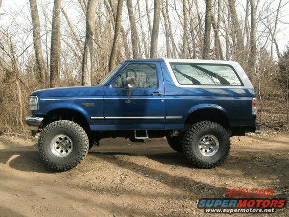 Blue lifted 1996 Ford Bronco parked on a dirt road with trees in the background