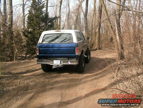Blue and white Ford Bronco with lifted suspension on a dirt path