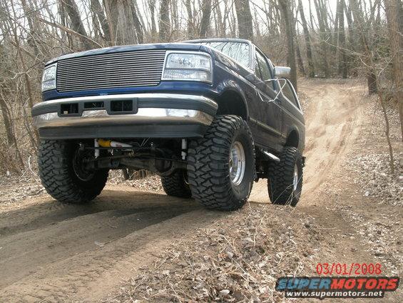 Blue 1996 Ford Bronco with chrome grille and large tires on dirt road