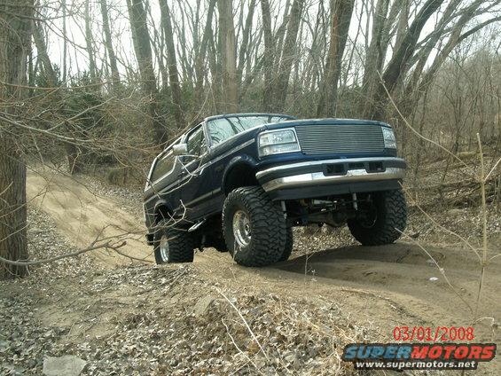 1996 Ford Bronco with large tires driving on a dirt trail