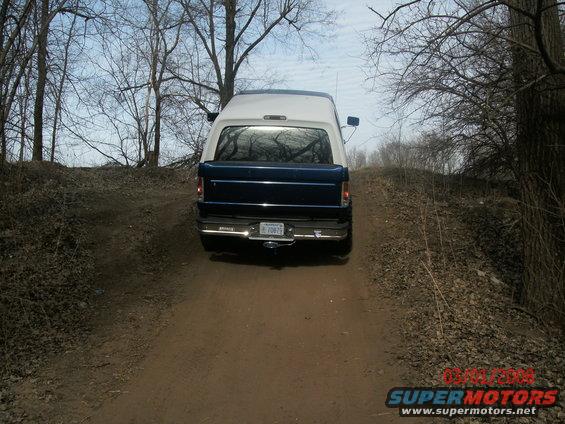 Rear view of a blue and white Ford Bronco driving up a dirt path. License plate is visible