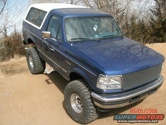 Blue Ford Bronco with white top, lifted suspension, and aftermarket grille