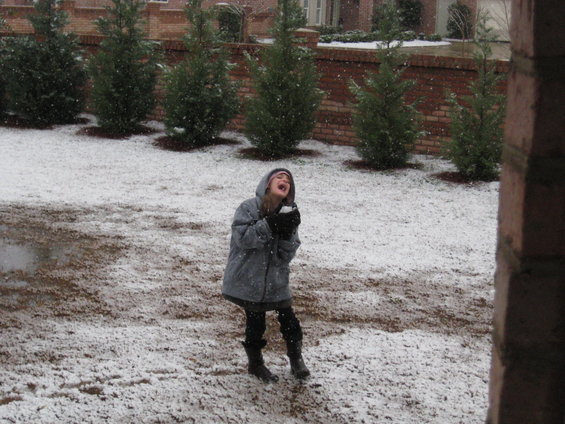 Child with mouth open catching snow, wearing a hooded jacket and boots