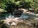 1993 Ford Bronco - A dark-colored Ford Bronco navigates a rocky stream surrounded by lush green trees.
