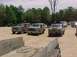 1993 Ford Bronco - A lineup of Ford Broncos and other trucks are parked in a dirt lot on a sunny day.