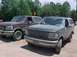 1993 Ford Bronco - Two Ford Broncos are parked side-by-side on a dirt lot with trees in the background.