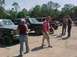 1993 Ford Bronco - Several people stand around parked vehicles, including a dark green Ford Bronco with roof-mounted lights.