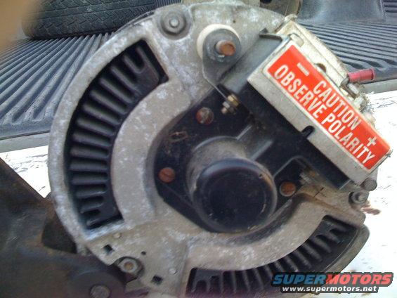 Alternator with red 'CAUTION OBSERVE POLARITY' sticker, showing fins and mounting points