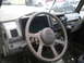 1987 Suzuki Samurai - The interior of a Suzuki Samurai shows its dashboard, steering wheel, and a CB radio, with other vehicles visible through the cracked winds…