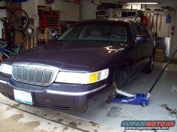 1999 Mercury Grand Marquis on a floor jack in a garage, front end visible
