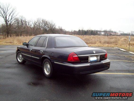 Dark blue sedan parked on wet asphalt, rear 3/4 view. Chrome trim, alloy wheels, tinted windows
