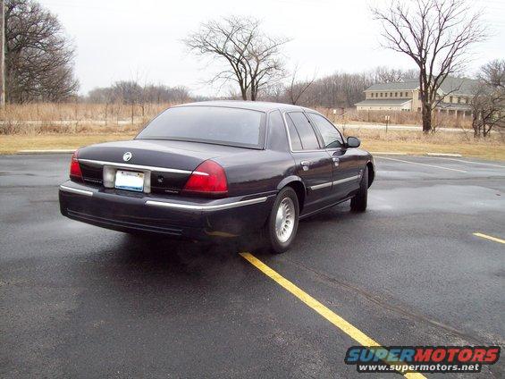 Dark sedan parked on asphalt with yellow lines. Rear view shows taillights and chrome trim