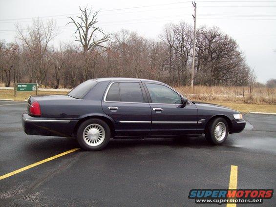 Side view of a 1999 Mercury Grand Marquis parked on asphalt with trees in the background