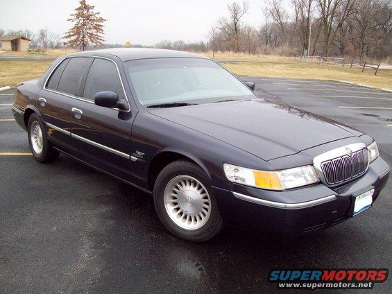 Dark blue sedan parked on wet asphalt, front quarter view. Chrome grille and trim visible