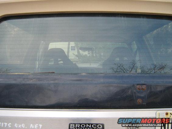1990 Ford Bronco rear window showing interior seats and reflection of a house