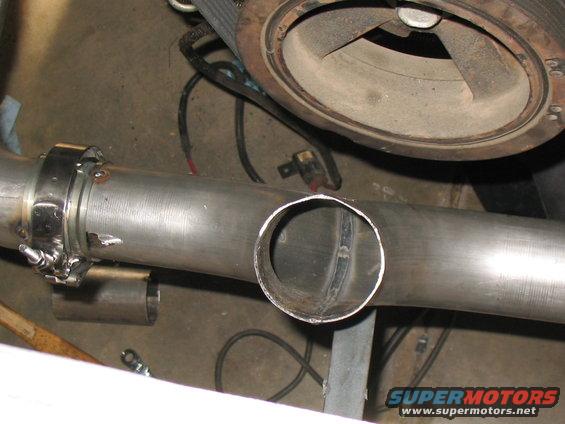 Custom exhaust pipe being fitted near a turbocharger. A section is cut out for a new connection