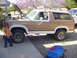 1982 Ford Bronco - A two-tone Ford Bronco sits outside with its hood up, next to a child and a blue wagon.