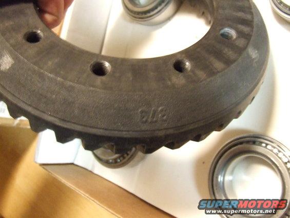 Close-up of a ring gear with part number 373 stamped on it, next to two bearings