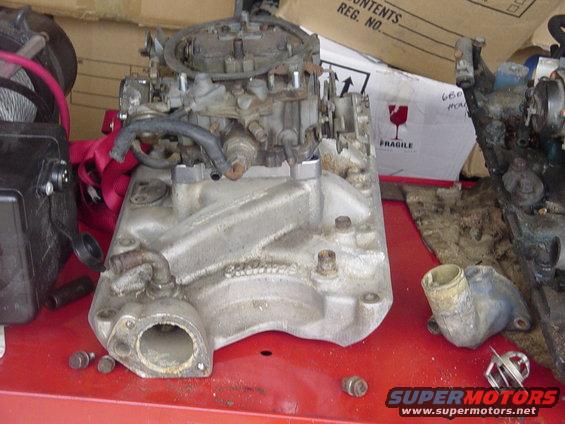 Engine intake manifold with carburetor and hoses, sitting on a red surface