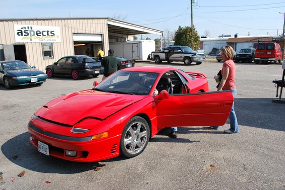 Red 1991 Mitsubishi 3000GT with driver's door open, parked outside a building
