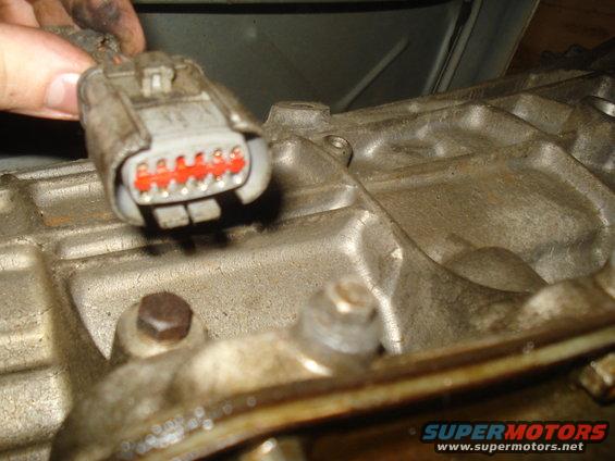 Gray electrical connector with red wire terminals plugged into a metal engine block
